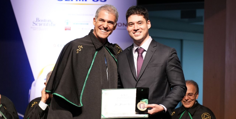 Imagem do Dr. Francisco Tustumi recebendo o prêmio Jovem Cirurgião de um senior